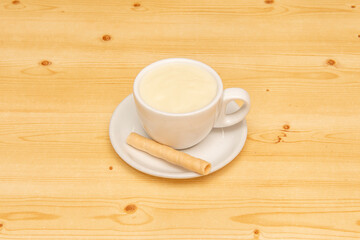 Cup of hot white chocolate with wafer on pine wood table