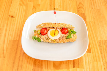 Sandwich with canned tuna with red cherry tomato, boiled egg and vegetables with seed bread on white plate