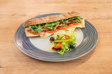 Ciabatta bread sandwich with fried chicken, kale, basile, caprese sauce, tomato and cheese with black olives, pickled piparra and lettuce