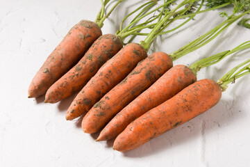 a bunch of fresh raw carrots with leaves on white table