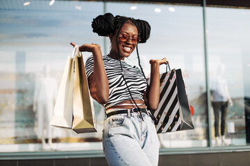 African American woman, wearing sunglasses, standing in a mall with shopping bags in her hands
