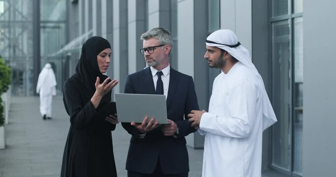 Happy multi-ethnic male and female proessionals having team business conference while working and speaking about business startup near the modern office. People looking on laptop and discussing