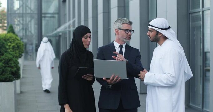 Waist up portrait view of multi-ethnic male and female professional managers working near the modern office. Beautiful arabian female gesturing and talking to team while man discussing with his