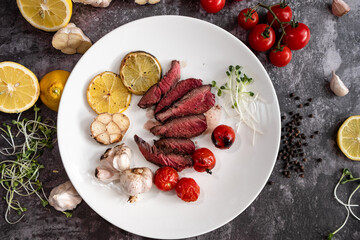 Sliced grilled thai steak served on white plate with grilled sliced lemon, tomatoes, garlic