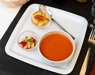 Traditional Spanish refreshing pureed soup Gazpacho from tomatoes served in white bowl with toasted bread and chopped fresh vegetables