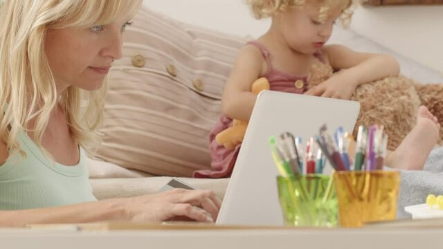compulsive online shopping, mother uses her credit card on the computer at home and neglects the daughter child who is unhappy and alone consoles herself with the stuffed animal
