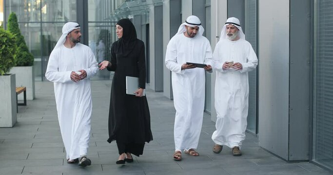Walking arab people wearing kandura on business location. Arabic businesspeople walking on the city streets wearing dish dasha. Arabian middle eastern smiling while walking and chatting