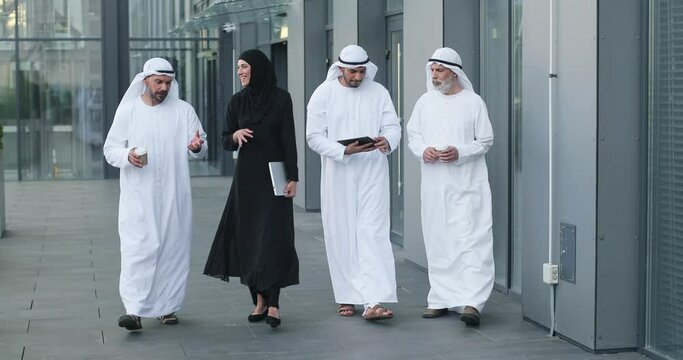 Walking arab people wearing kandura on business location. Arabic businesspeople walking on the city streets wearing dish dasha. Arabian middle eastern smiling while walking and chatting