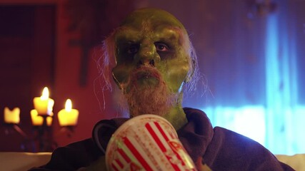 Green monster watching TV and eating popcorn at home at night, closeup low angle