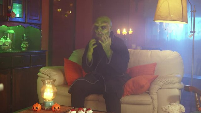 Green monster watching a horror movie on TV at home at night
