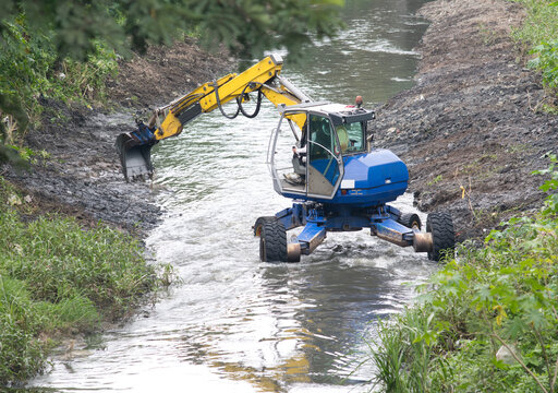 Excavator performing river dredging and clearing up the river banks.
