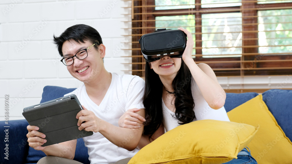 Wall mural Happy asian couple play virtual reality simulation game while sitting on sofa at home living room, People and technology