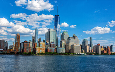 Obraz premium Panoramic view on New York City skyline from sea side. Blue sky and puffy clouds above skyscrapers.