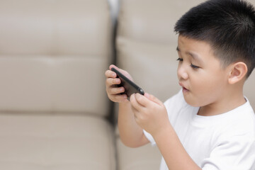 Happy little boy having fun playing game on mobile phone, Preschool kid sitting on sofa with smiling face watching cartoon on smartphone, Child using cell phone while relaxing at home