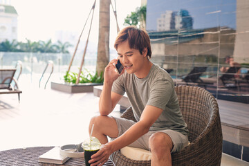 Handsome man drinking coffee and using the phone by the pool.