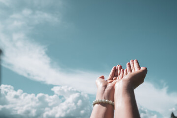 Woman hands place together like praying in front of blue sky background.