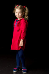 Cute blonde little girl standing on black backdrop