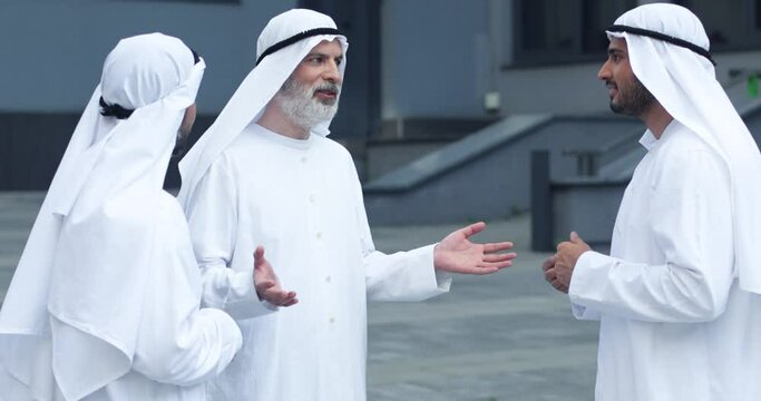 Waist up portrait view of the confident senior sheikh chatting with his business partners and gesturing while standing at the street. Business concept