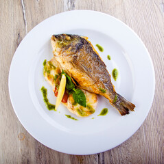dorado fish on a plate with garnish and pesto sauce top view
