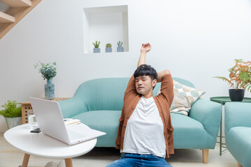 Asian man sitting on the floor and playing on the computer, feeling tired