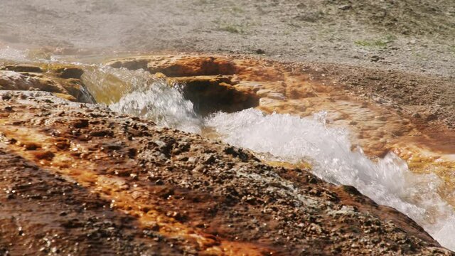 Hot springs in world famous Yellowstone National Park 4K. Slow motion hot water stream flowing down from volcanic geyser basin by iron and cooper mineral elements reach surface in vibrant orange color
