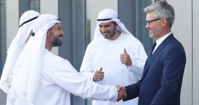 We made a deal. Full length view of successful two business partners shaking hands. They are standing at the street near their colleagues. People are gesturing at the background