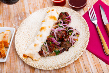 Delicious grilled pork shashlik garnished with fresh purple onion slices served with sauces and thin lavash on wooden table