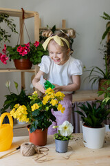 a little blonde girl with a headband on her head and wearing work gloves sprays from a bullet dispenser or waters indoor flowers. Home gardening, caring houseplants. Space for text. High quality photo