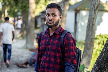 A small beard young boy is standing wearing a dark red shirt and his background is blurred.