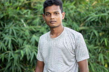 A small beard young boy is standing wearing a grey t-shirt and his background is blurred.