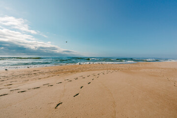 Empty sand beach, turquoise colored ocean, footsteps on sand, and cloudy sky on background.