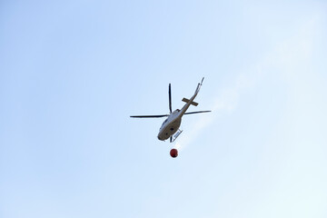 Firefighting helicopter transporting water to extinguish a fire. Hazard concept