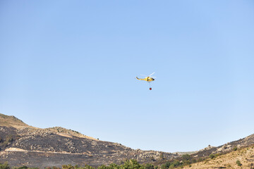 Fototapeta na wymiar Firefighting helicopter transporting water to extinguish a fire. Hazard concept