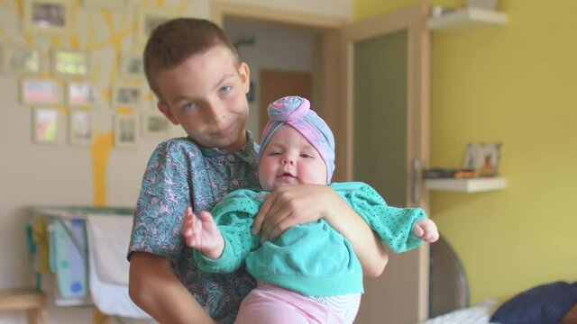 Posing children. A teenager holds a little girl sister in the room. He kisses her. Close relationships are close relatives. Focus of attention to the camera. 