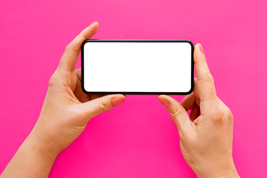 Mobile phone with empty white screen held in hands horizontally on bright pink background