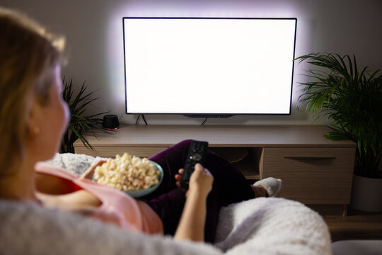 Woman watching TV at home, empty white TV screen mockup