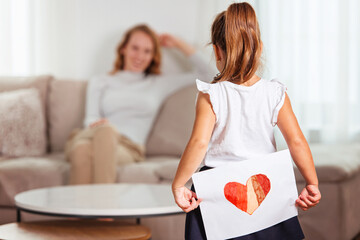 Cute little girl giving a heart-drawing to her mother