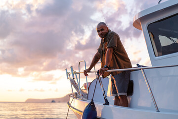 Young african american man relaxing on a sailboat in open sea at sunset