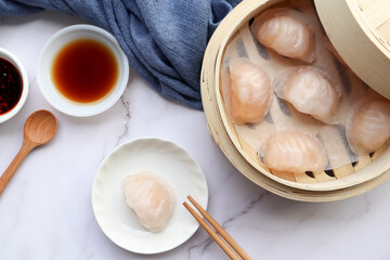 Shrimp dumpling Dim Sum in a small plate and in bamboo steamer with sauce and chopsticks - Flat lay of Chinese food called Har Gow