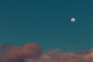 full moon with pink fluffy clouds underneath it in the blue sky at dusk