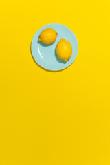 Trendy bright yellow summer citrus background with whole lemons on a blue round plate and empty space for text. 
