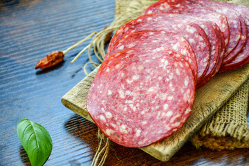 Italian  dried thinly sliced   artisan  pork salami Milano , parmesan cheese, grissini , tomatoes   and fresh basil on wooden background .Rustic  home made italian snack.