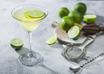 Gimlet Kamikaze cocktail in martini glass with lime slice and ice on light board with fresh limes...