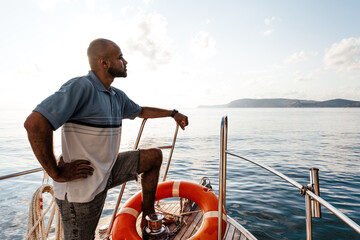 Young african american man relaxing on a sailboat in open sea at sunset