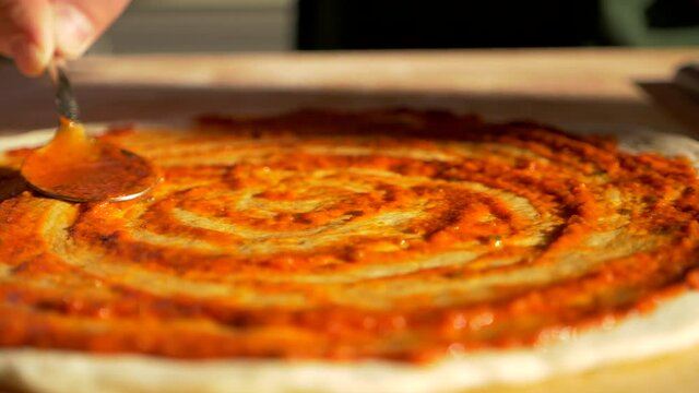 Italian food restaurant chef baker cook spread tomato sauce of pizza pie pastry dish roasting. Spoon filling of tomatoes gravy on floured piece of dough before baking in oven. Tasty foodstuff cuisine.