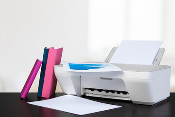 Compact home printer on desk with books against blurred background
