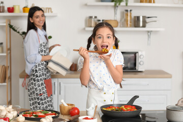Little girl with mother cooking in kitchen at home