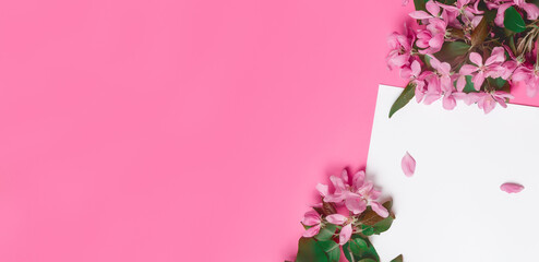 Top view of blank sheet of notebook and branches of apple blossoms on pink background. Copy space.