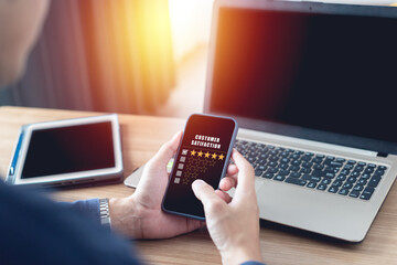 Smart businessman holding a mobile phone and rating satisfaction 5 star. laptop computer tablet to work from home This allows you to communicate with people around the world anytime, anywhere