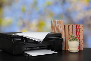 Compact home printer on desk with books against blurred background